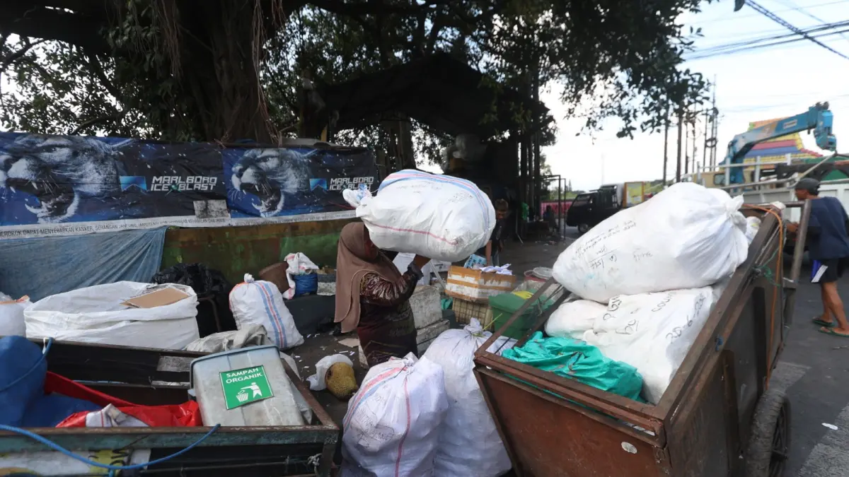 MAKSIMALKAN PENGELOLAAN SAMPAH: Seorang warga memasukkan sampah ke gerobak di TPS Embong Brantas, Kota Malang, kemarin. Dewan ingin pengelolaan sampah tidak hanya menunggu realisasi PSEL. (Foto: Darmono/Radar Malang)