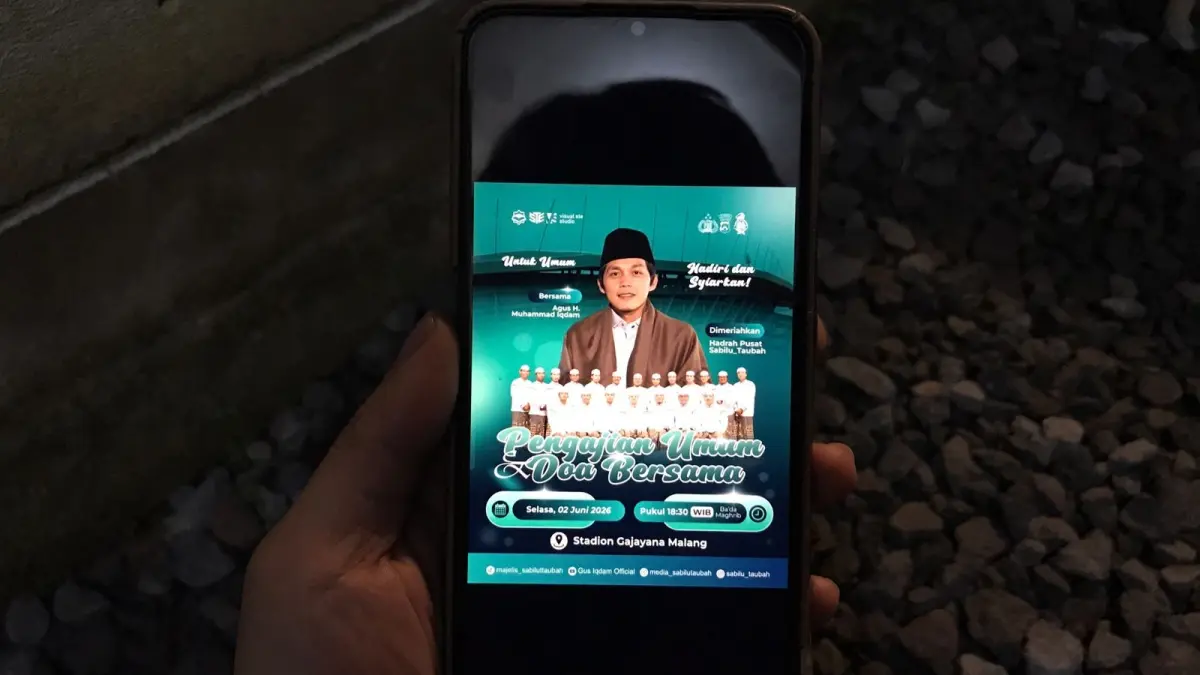 Seorang warga melihat poster pengajian Gus Iqdam yang digelar 2 Juni 2026 di Stadion Gajayana. (Aditya Novrian/Radar Malang)