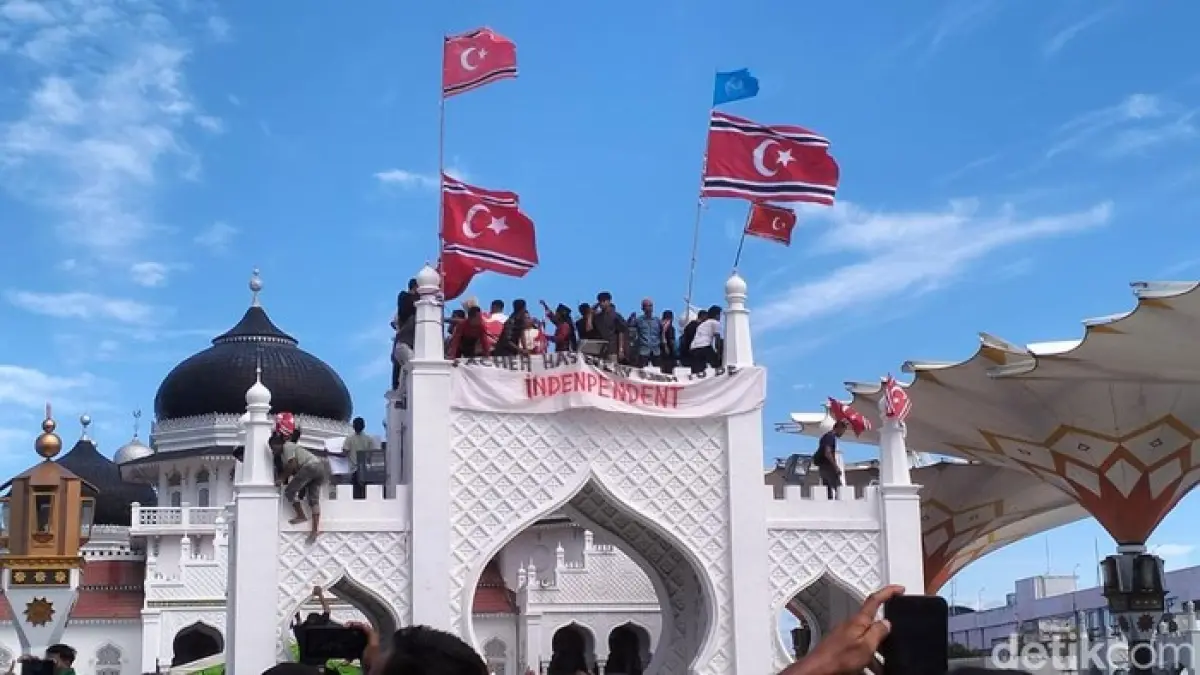 Sejumlah massa menaiki gapura di halaman Masjid Raya Baiturrahman, Banda Aceh, Sabtu (15/8/2026), untuk mengibarkan bendera Bulan Bintang di sela-sela peringatan Hari Damai Aceh yang berakhir ricuh. Forum Komunikasi Pimpinan Daerah (Forkopimda) Aceh menduga ada pihak tertentu yang menggerakkan aksi tersebut.  (Foto: Agus Setyadi/detikSumut / Sumber: detikcom)