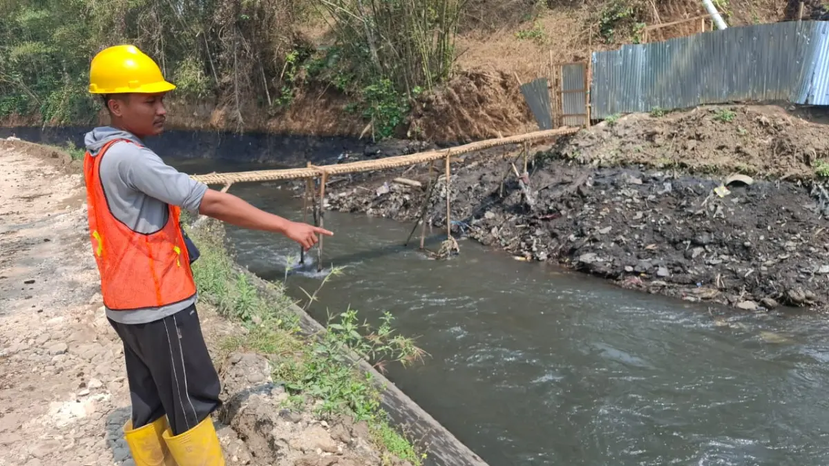 Seorang pekerja menununjuk air sungai yang tercemar