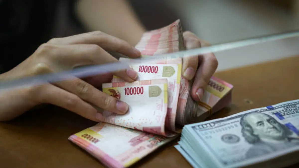 Ilustrasi Seorang karyawan menghitung uang kertas pecahan 100.000 rupiah, sementara segepok uang kertas pecahan 100 dolar AS tergeletak di meja layanan sebuah tempat penukaran mata uang di Indonesia. (Getty Images/Dimas Ardian/Bloomberg)