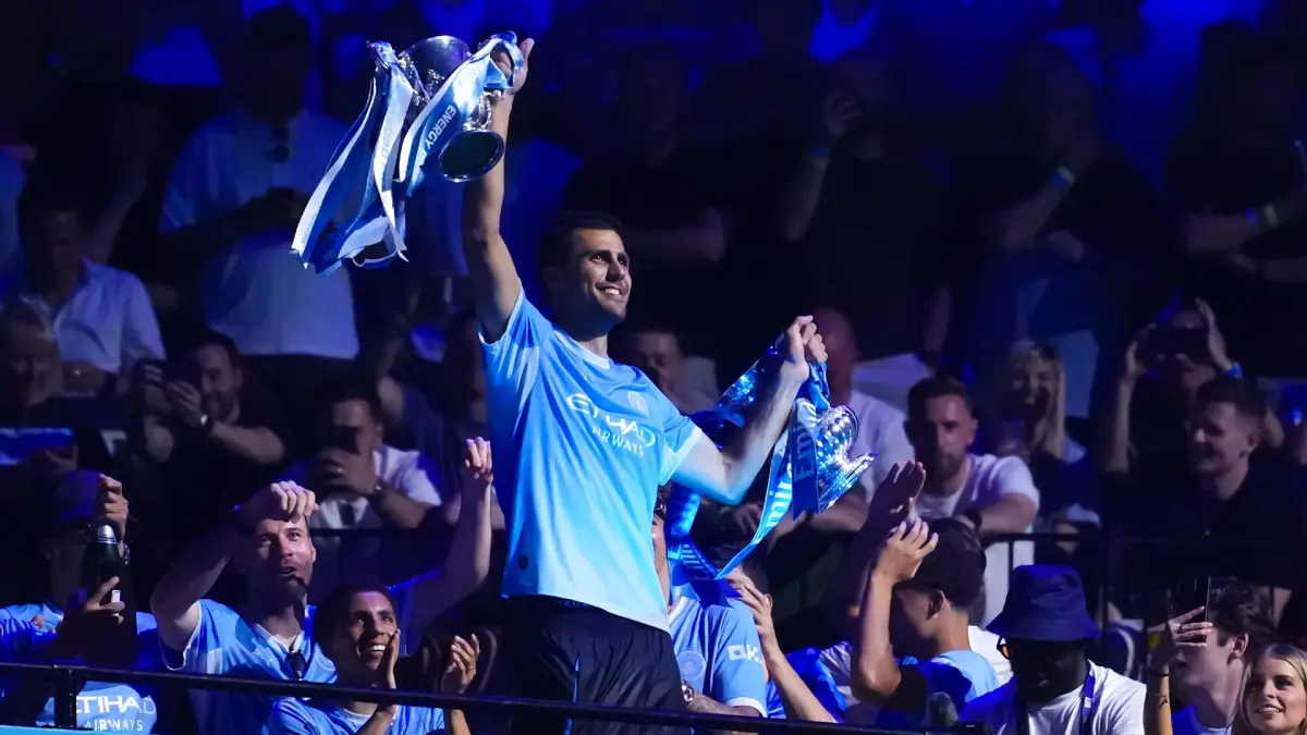 Rodri memamerkan trofi Piala FA dan Piala Carabao dalam acara parade yang tak terlupakan yang digelar di Co-op Live pada Mei 2026.
Sumber: Website/mancity.com