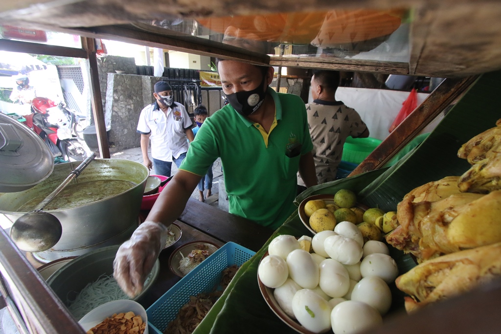 Zainuri tengah meracik soto di mangkuk yang akan disajikan ke pembelinya.