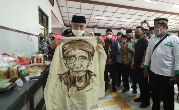 Bupati Malang HM Sanusi menunjukkan lukisan bordir bergambar KH Maimun Zubair (Mbah Mun) yang dibeli dari salah satu UMKM peserta workshop di Unisma, Minggu (20/9). (Laoh Mahfud/Radar Malang)