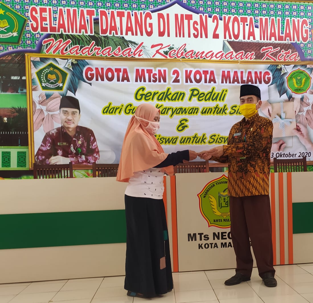 Kepala MTsN 2 Kota Malang Dr Subhan SPd MSi (kiri) menyerahkan bantuan secara simbolik kepada wali murid. (Errica V / Radar Malang)