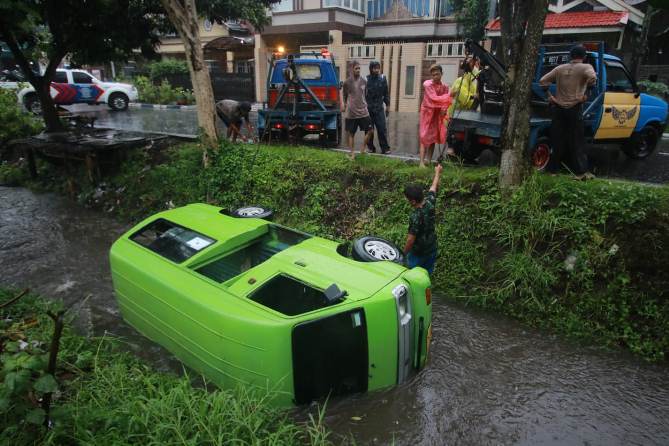 Angkot jurusan Lawang-Arjosari dengan nomor polisi N 1554 UE yang masuk sungai siang tadi di Jalan Panji Suroso tengah dievakuasi, Rabu (12/30). (Laoh Mahfud/Radar Malang)