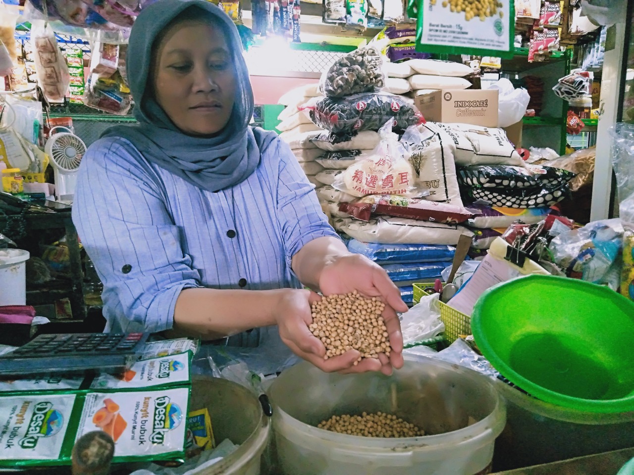 Salah seorang pedagang pasar Oro-Oro Dowo Kota Malang menunjukkan kedelai yang dijual di bedaknya. (Imam N/Radar Malang)