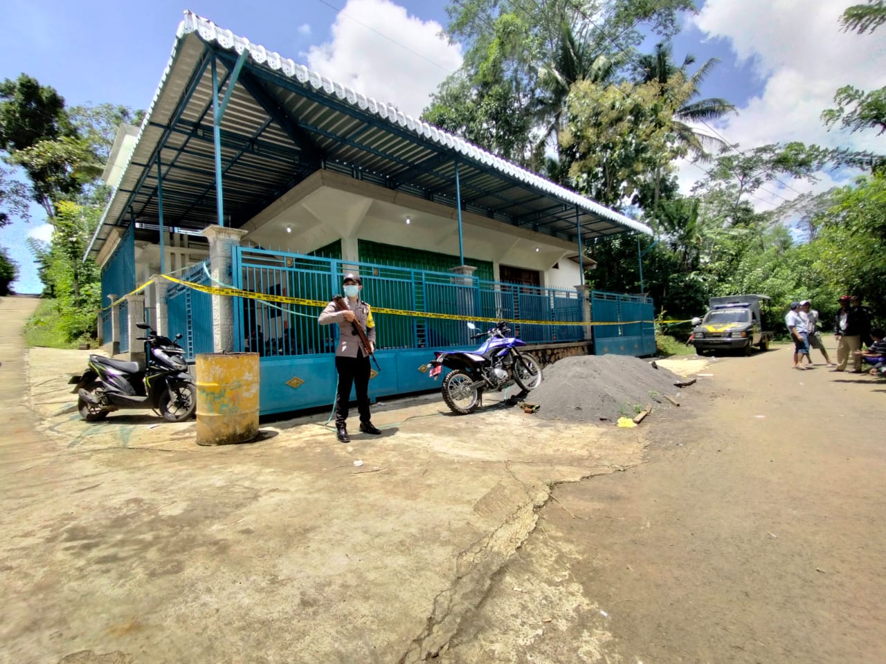 Polisi berjaga-jaga di depan rumah tempat jenazah Tamin ditemukan di Desa Bumirejo, Kecamatan Dampit, Kabupaten Malang. (Ahmad Fikyansyah/Radar Malang)