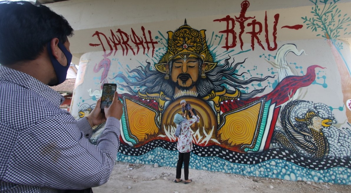 M Ubaidillah memfoto anak dan istrinya di depan mural di flyover Kedungkandang. Kota Malang.(Laoh Mahfud/Radar Malang)