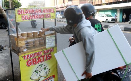 Pengendara sepeda motor mengambil nasi gratis di depan oulet Century Computer, Kota Malang. (Darmono/Radar Malang)