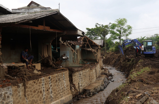 Seorang warga tampak meratapi rumahnya yang hancur di Dusun Beru, Desa Bulukerto, Kota Batu. Sementara petugas menggunakan alat berat meratakan material yang berserakan di pinggir sungai. (Darmono/Radar Malang)