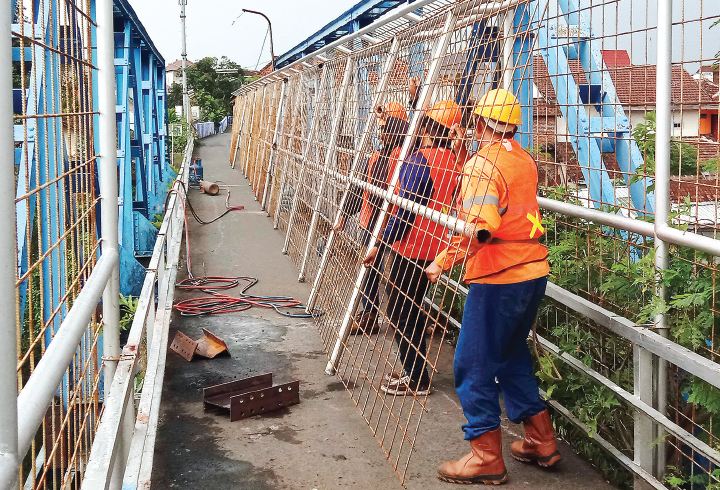 Pekerja tengah memindahkan pagar pengaman yang baru dipotong untuk mengawali proyek pelebaran jembatan Pelor. Pengerjaan proyek ditarget tuntas akhir tahun. (Darmono/Radar Malang)