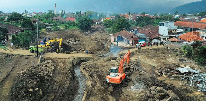 Para pekerja membersihkan material batu, kayu dan lumpur di Desa Bulukerto, Kecamatan Bumiaji, menggunakan alat berat Selasa lalu (9/11). (Darmono/Radar Malang)