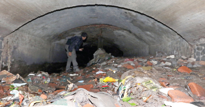 Pendangkalan saluran air yang melintang di bawah Jalan Letjen Sutoyo sudah sangat parah. Ada lumpur, endapan tanah, bekas material bangunan, hingga sampah. (Darmono/Radar Malang)