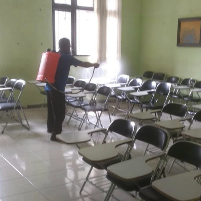 DARING LAGI: Petugas menyemprotkan cairan disinfektan di salah satu ruangan yang digunakan untuk kuliah di kampus UM. (andika/radar malang)