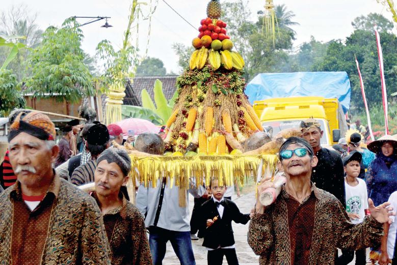SEMPAT TERHENTI: Gunungan berisi buah dan hasil pertanian diarak warga ke lokasi pagelaran wayang di Dusun Sembon, Desa Ngajum, Kecamatan Ngajum, kemarin siang (13/6). (DARMONO / RADAR MALANG)