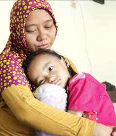 DALAM PERAWATAN: Queensha Humaira Dzawata Afnan duduk di pangkuan ibunya, Rachma Eka Jumaningsih Iskandar Alam, setelah lelah bermain di rumahnya kemarin siang (29/10). (DARMONO/RADAR MALANG)
