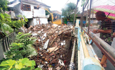 SUDAH LAMA RUSAK: Pekerja merobohkan rumah di Jalan Raya Serayu Selatan  Nomor 18A menggunakan ekskavator kemarin siang. Sehari sebelumnya, tembok  samping rumah itu roboh akibat tanah di bawahnya longsor ke sungai.
