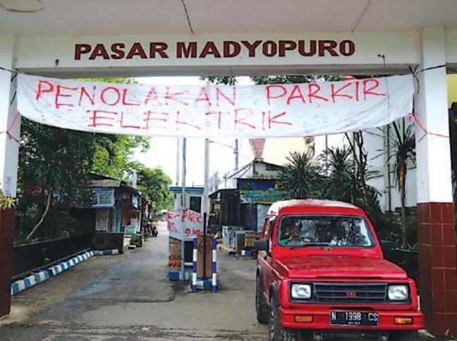 berdalih tanPa sosialisasi: spanduk penolakan terpampang di gapura jalan utama menuju Pasar madyopuro, kemarin (29/12). Fasilitas pendukung e-parking juga disegel menggunakan spanduk. - Darmono Radar Malang