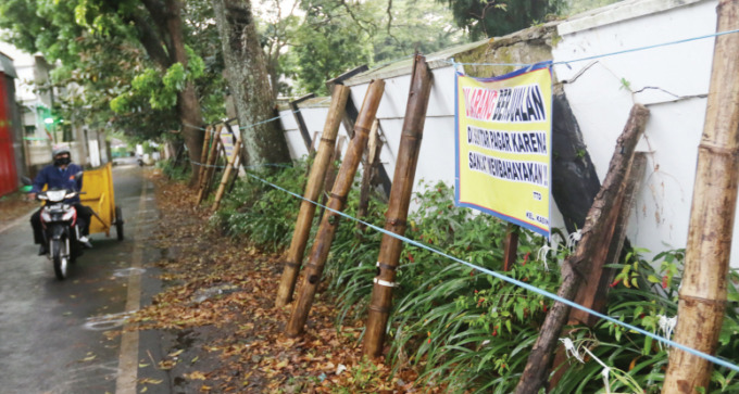 MIRING 45 DERAJAT: Puluhan bambu dipasang warga untuk menahan tembok pagar TPU Kasin yang miring sejak beberapa bulan lalu supaya tidak roboh. Pemkot Malang baru melakukan perbaikan pada Maret mendatang.
