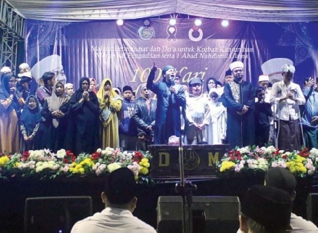 BERMUNAJAT: Khodimul Majelis Darul Musthofa Malang Romo KH Ahmad Soeroso bin Soedri (pegang mic) bersama keluarga korban tragedi Kanjuruhan melantunkan salawat di depan Gedung KNPI Kota Malang, tadi malam. Doa untuk korban tragedi Kanjuruhan juga dipanjat