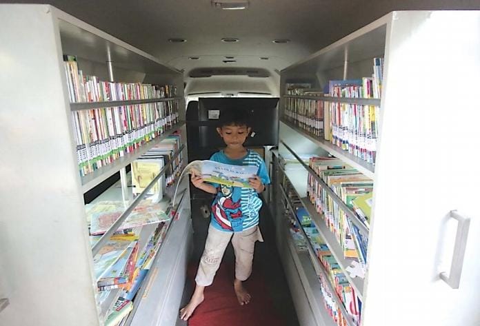 GENJOT LITERASI: Seorang bocah membaca buku dongeng di dalam mobil Perpustakaan Keliling kemarin (27/1). - Suharto/radar malang