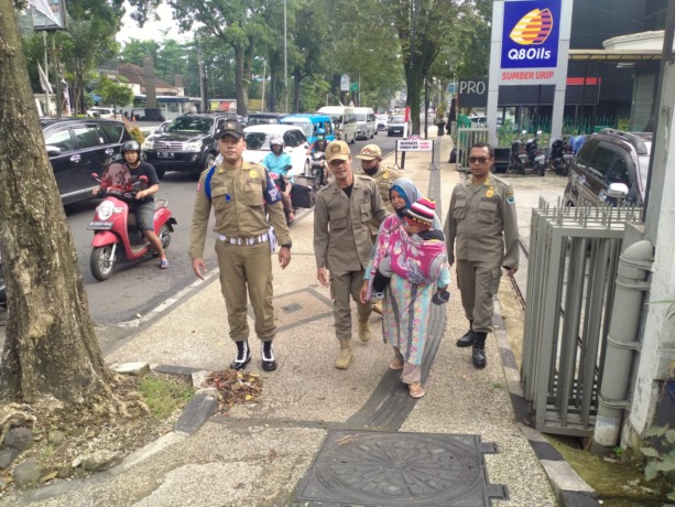 MELANGGAR PERDA: Petugas Satpol PP Kota Malang mengamankan perempuan yang mengemis di Jalan Letjen Sutoyo sambil menggendong anak kecil. (dokumen radar malang)