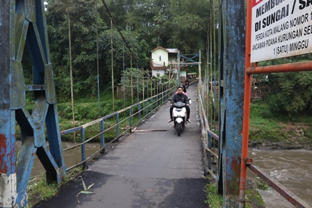 INFRASTRUKTUR: Pengendara melintasi jembatan gantung di Mergosono Gang 5 kemarin (6/2). Jembatan tersebut mulai diperbaiki Pemkot Malang.