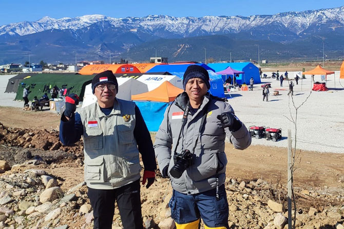 MISI KEMANUSIAAN: Zakarija Achmat (kiri) dan Rindya Fery Indrawan berdiri dengan latar belakang rumah sakit lapangan yang diririkan Emergency Medical Team Indonesia di Kota Iskandarun, Turki.(ZAKARIJA FOR RADAR MALANG)