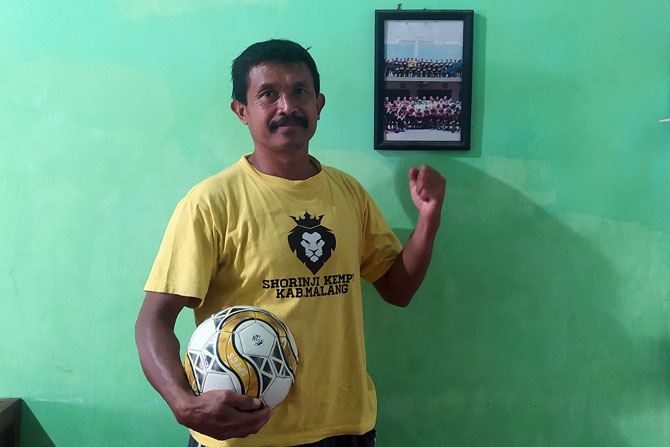 JUJUKAN PESEPAKBOLA: Akhmad Khamim berpose di depan foto tim PSBK Blitar dan Persepam Madura yang sempat disinggahinya. (Galih R Prasetyo/Radar Malang)