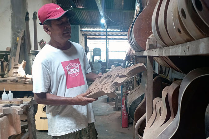 CIRI KHAS: Dariatmo menunjukkan proses pembuatan gitar elektrik yang dilengkapi ukiran manual di rumahnya. (HANIFUDDIN MUSA/RADAR MALANG)