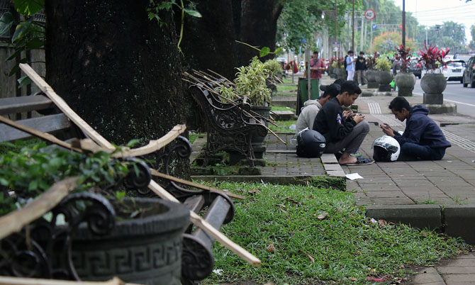 LESEHAN : Para pemuda yang nongkrong di Jalan Besar Ijen terpaksa lesehan di pedestrian karena bangku taman disegel. (Suharto/Radar Malang)