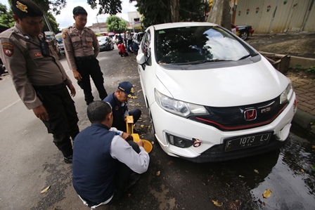 Personel Dishub Kota Malang menggembok mobil yang parkir di Jalan Pattimura.