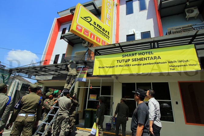 IMBAS KELUHAN WARGA: Petugas Satpol PP Kota Malang memasang banner berisi tulisan ”DITUTUP SEMENTARA” di kanopi lantai satu Smart Hotel kemarin siang (22/5). (Suharto/Radar Malang)