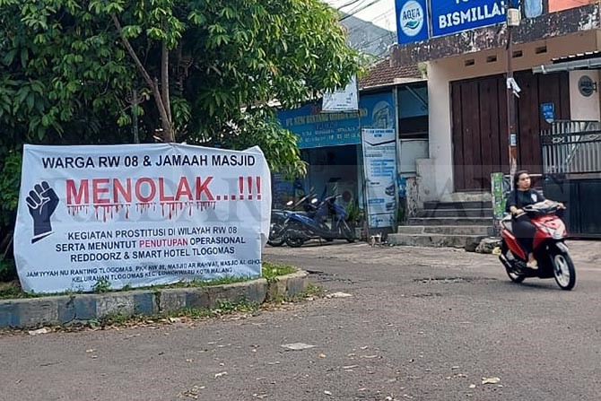 DALAM PENGAWASAN: Spanduk berisi penolakan prostitusi online di dua tempat menginap dipajang warga RW 08 Keluraan Tlogomas, Kecamatan Lowokwaru sejak Jumat lalu (12/3).(BIYAN MUDZAKY HANINDITO/RADAR MALANG)