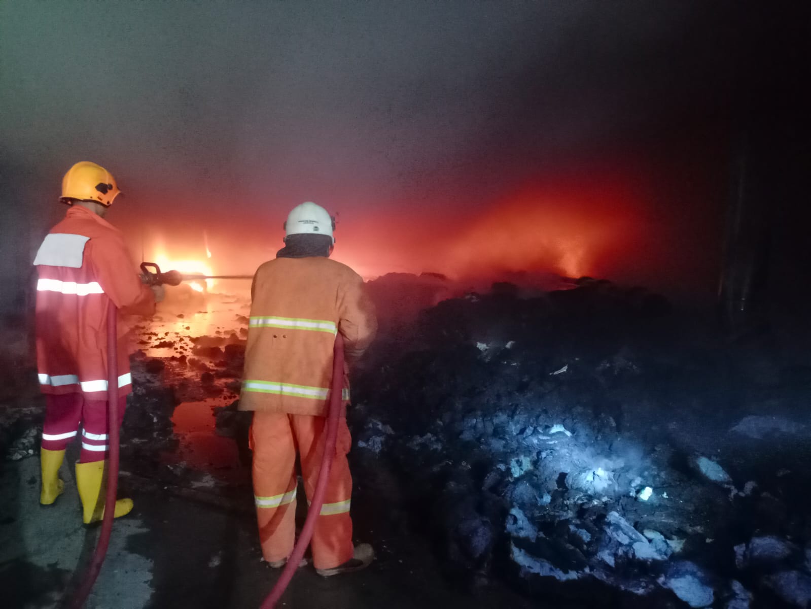 PENANGANAN: Petugas melakukan upaya pemadaman dan memasang garis polisi di ruang produksi UD Merak Utama Gloves, Jalan Raya Desa Perning, Kecamatan Jetis, Selasa (18/7) malam.