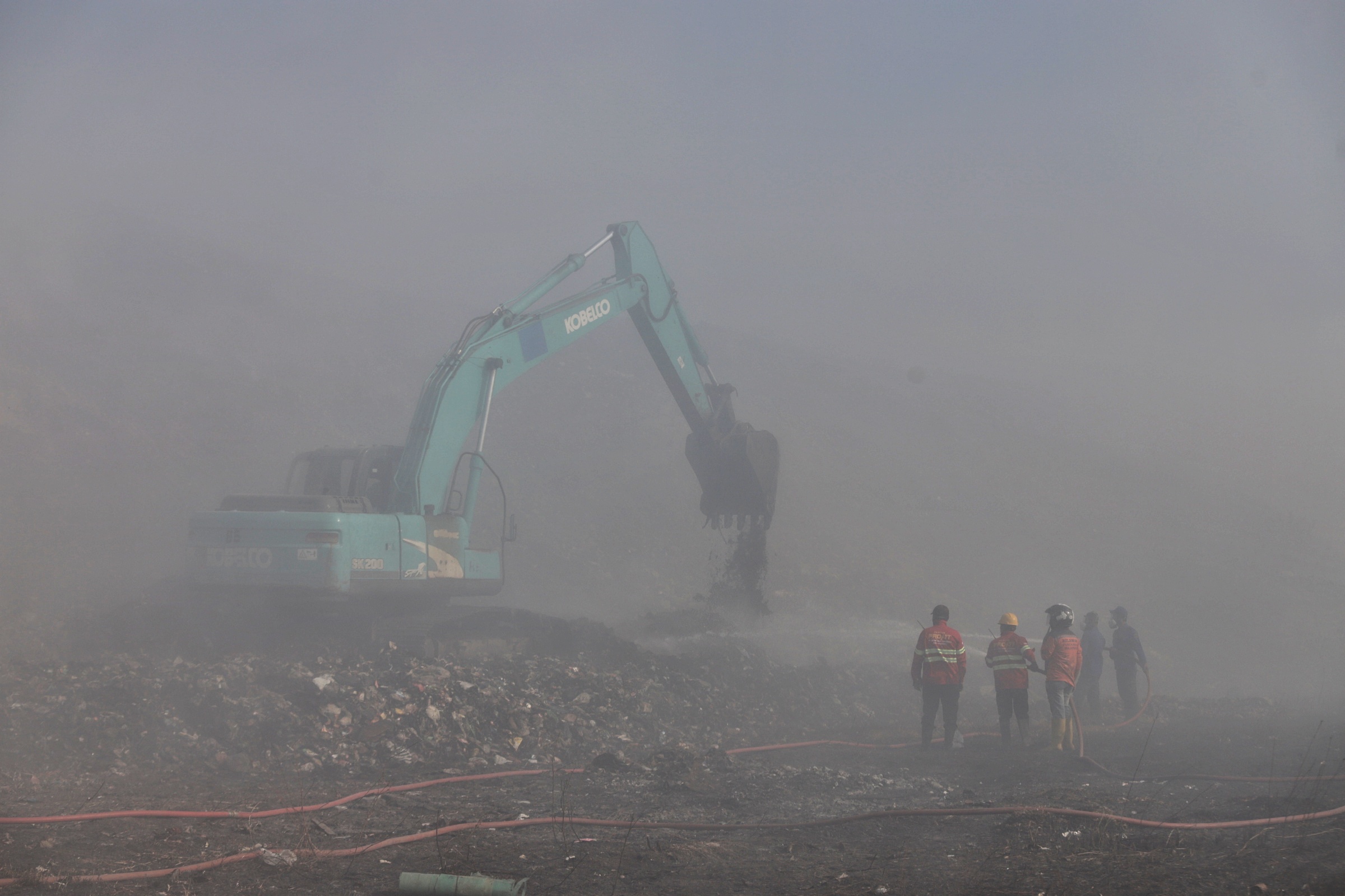 BELUM USAI:Petugas pemadam dibantu alat berat berjibaku memadamkan api ditengah debu dan asap tebal di TPA Randegan Kota Mojokerto kemarin.