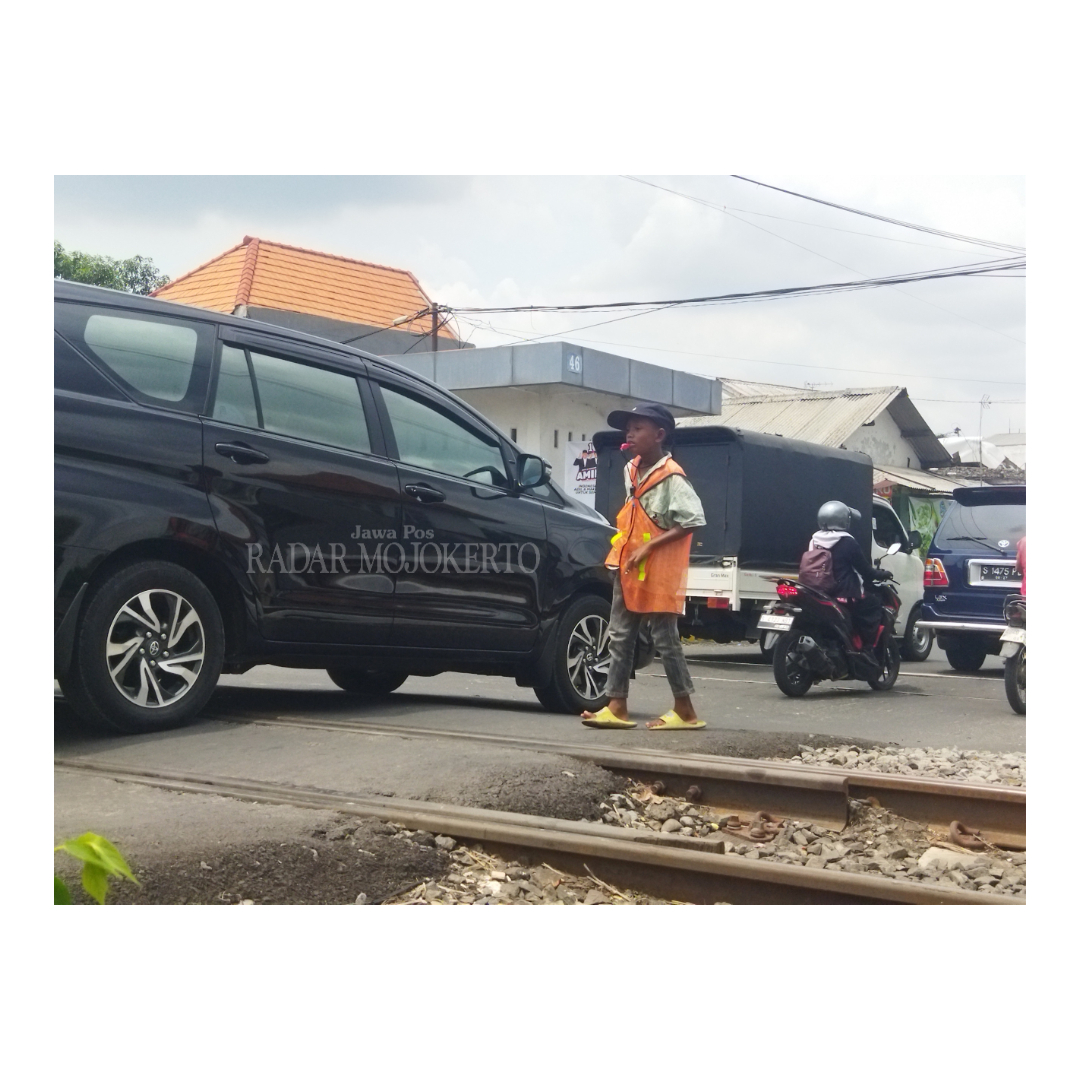 BERJUANG SENDIRI: Mamat, saat membantu menyeberangkan pengendara di perlintasan KA Jalan Brawijaya, Kelurahan Miji, Kecamatan Kranggan, Kamis (14/12).