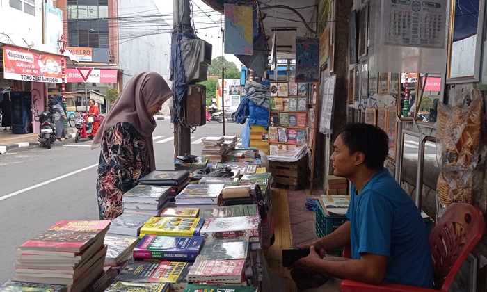 TURUN DRASTIS: Pembeli mengamati tumpukan buku yang dijual Yosef, di Jalan Niaga, Kelurahan Sentanan, Kecamatan Magersari, Kota Mojokerto, Rabu (10/1). (foto: Afi for Radar Mojokerto)