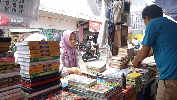 MELAYANI: Yosef mengambilkan buku yang dicari pembeli di tokonya, Jalan Niaga, Kelurahan Sentanan, Kecamatan Magersari, Kota Mojokerto, Rabu (10/1). (foto: Wilda for Radar Mojokerto)