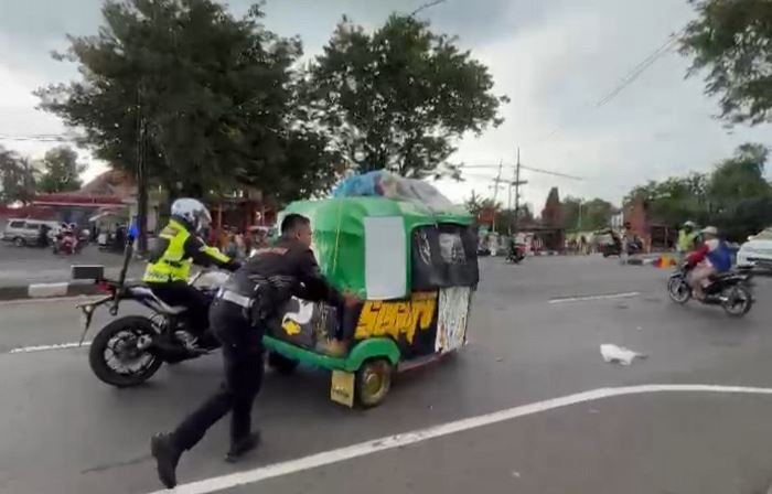 DIBANTU: Petugas Satlantas Polres Mojokerto mendorong bajai pemudik dari Jakarta yang mogok di Desa Jatipasar, Trowulan, Mojokerto. Jumat (12/4). (foto: Moch. Chariris)