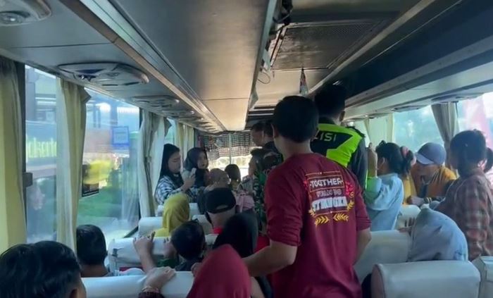 PENUH DAN SESAK: Petugas menurunkan penumpang yang pingsan dari dalam bus PO Harapan Jaya di Rest Area Gunung Gedangan, Kecamatan Magersari, Kota Mojokerto. (foto: Moch. Chariris)
