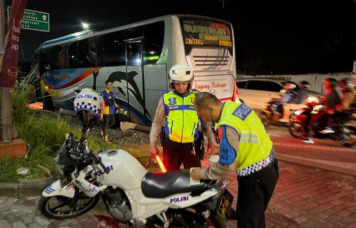 DITINDAK: Dua petugas Satlantas Polres Mojokerto Kota menilang bus PO Sugeng Rahayu karena melanggar marka jalan di Jalan Raya Bypass Gunung Gedangan, Kota Mojokerto, Minggu (14/4) malam.
