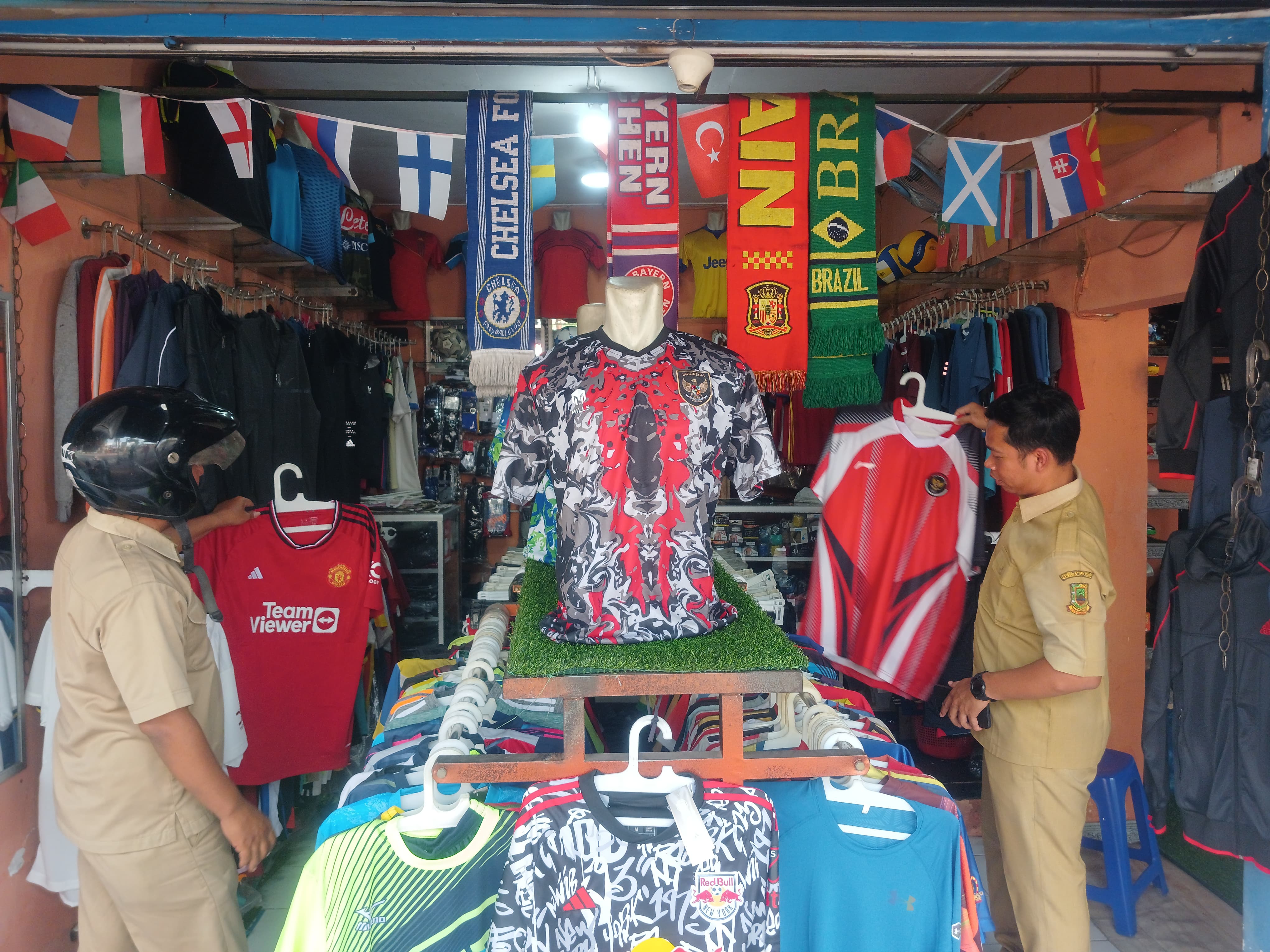 KECELE: Dua pegawai dinas di Kota Mojokerto memilah baju klub sepak bola setelah kehabisan jersey timnas di toko kostum olahraga Vandist Sport, Jalan Pahlawan, Kota Mojokerto, Senin (29/4) siang.