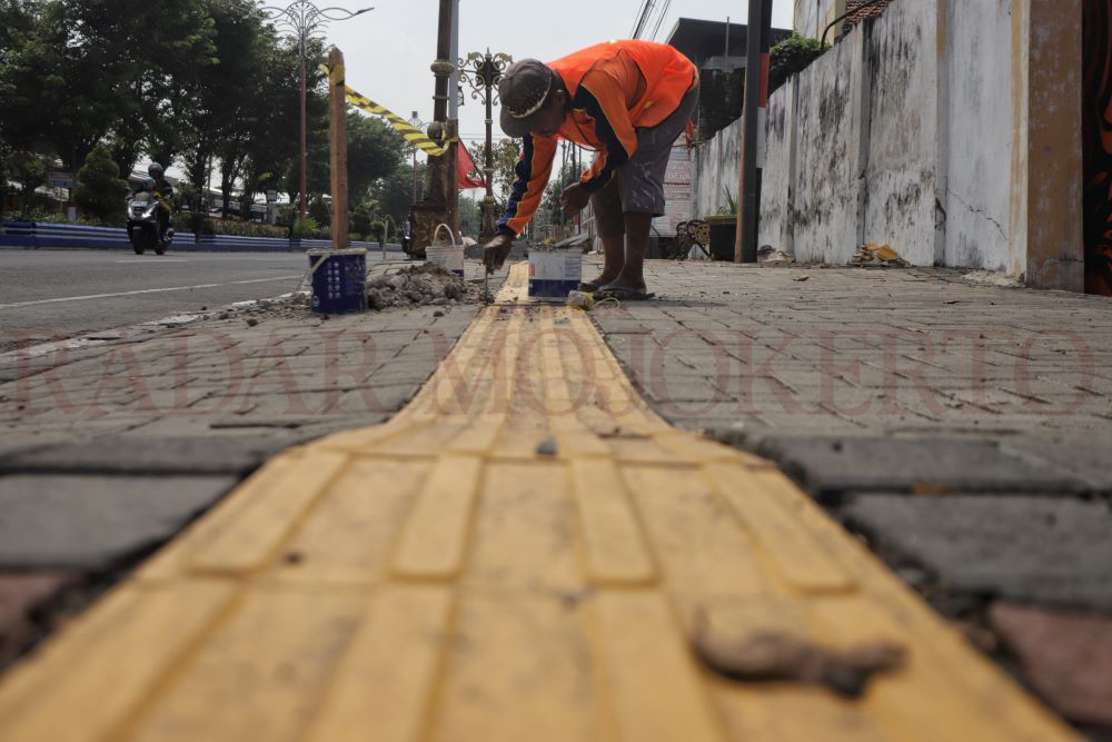 TAMBAL SULAM: Seorang pekerja tengah melakukan perbaikan tambal sulam pada jalur difabel di Jalan Pahlawan, Kota Mojokerto yang alami kerusakan.