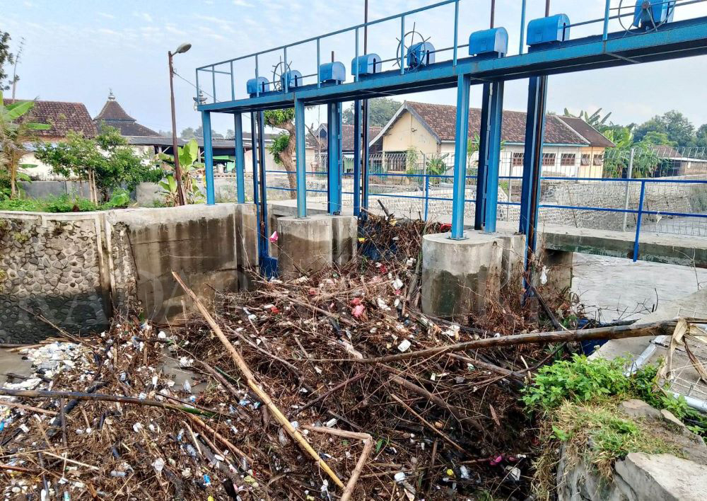 MENUMPUK: Pintu DAM sungai Sadar di Desa Sadartengah, Kecamatan Mojoanyar tersumbat sampah ranting pohon kiriman dari hulu.
