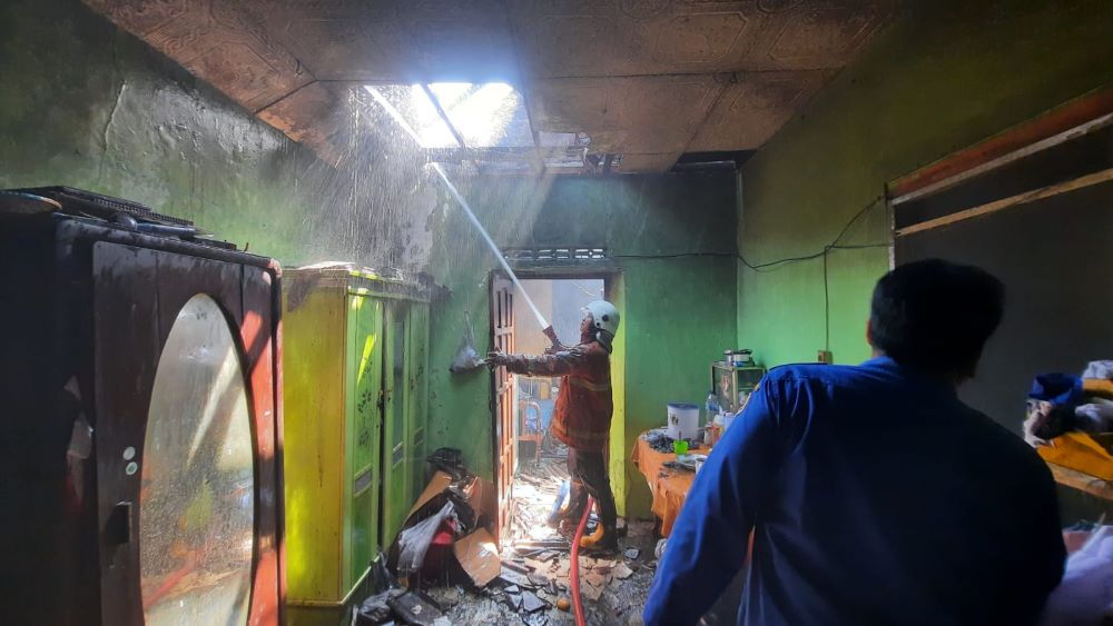 LUDES: Petugas damkar melakukan pembasahan di area belakang rumah yang ludes terbakar, Kamis (25/7) pagi.