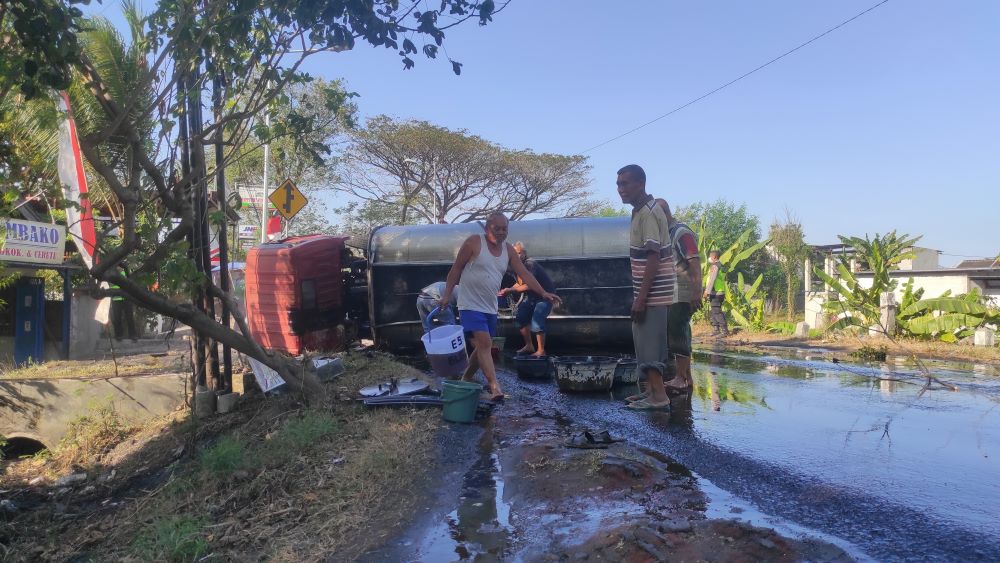 MANFAATKAN KESEMPATAN: Warga berebut minyak goreng curah yang tumpah dari truk tangki yang terguling di Jalan Raya Desa/Kecamatan Jetis, Senin (12/8) siang.
