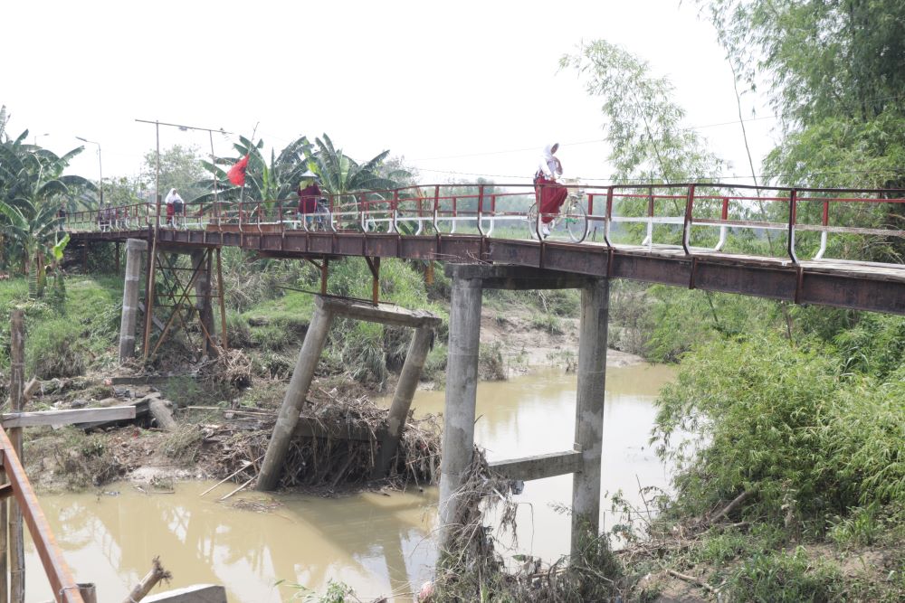 DARURAT: Seorang pelajar memanfaatkan jembatan darurat berkonstruksi bambu yang dibuat secara swadaya oleh masyarakat di Desa Talunblandong, Kecamatan Dawarblandong.