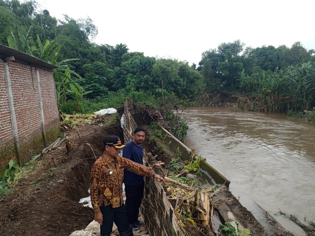 DETEKSI BENCANA: Kades Sambiroto Ahmad Farid Ainul Alwi bersama Camat Sooko Masluchman mengecek kondisi salahs satu titik tanggul Sungai Brangkal yang kritis.